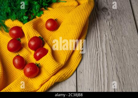 Chery Tomaten mit Grüns auf einem gelben Handtuch stehen auf einem Holztisch mit Bereich für Text Stockfoto