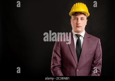 Portrait des Ingenieurs Architekt Baumeister mit blonden Haaren trägt einen gelben Schutzhelm in Burgunder Jacke, weißes Hemd und schwarze Krawatte posiert auf ist gekleidet Stockfoto