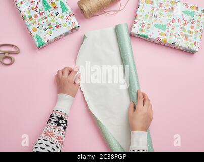 Zwei weibliche Hände eine Rolle Geschenkpapier, neben zwei Geschenke, rosa Hintergrund entfalten, Überraschungen vorbereiten Stockfoto