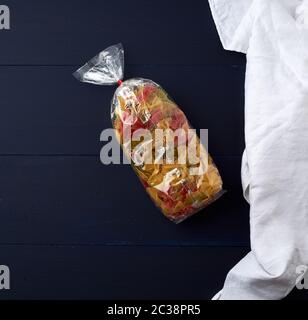 Transparente Zellophan Beutel mit Raw bunte Nudeln in Form von Bögen auf blauem Holz- Oberfläche, kopieren Raum Stockfoto