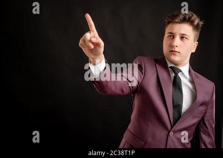 Jurastudent mit blonden Haaren in Burgunder Jacke, weißes Hemd und schwarze Krawatte gekleidet drückt eine virtuelle Taste posiert auf isoliertem schwarzen Hintergrund mit Co Stockfoto