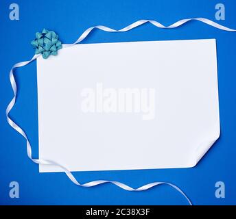 Leeres weißes Blatt Papier mit einer gewellten Ecke und White Ribbon auf blauem Hintergrund, kopieren Raum Stockfoto