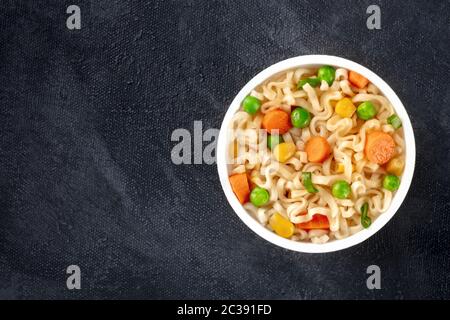 Ramen Tasse, Instant Soba Nudeln in einem Plastikbecher, mit grünen Erbsen und Karotte, über Kopf Schuss mit einem Platz für Text auf einem schwarzen Bac Stockfoto