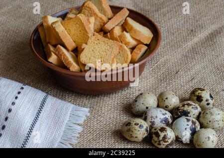 Stillleben mit Croutons und rohen Wachteleiern auf Eimer. Eine Tonschale mit kleinen quadratischen Paniermehl und einer Gruppe Wachteleier. Einfache gesunde Lebensmittel. Sel Stockfoto