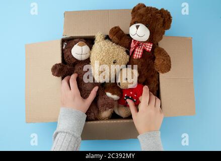 Braun Karton mit verschiedenen Teddybären, Ansicht von oben, Konzept der Hilfe und Freiwilligenarbeit, weibliche Hand füllt eine Kiste mit Spielzeug Stockfoto