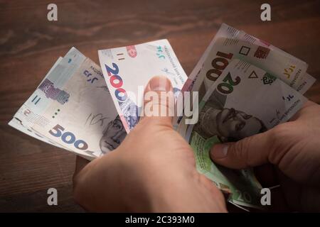 Kaukasischer Mann zählt Papiergeld. Männliche Hände halten Packung der neuen ukrainischen Banknoten, hrywnias auf Holztisch. Cash Money-Konzept. Investitionskonzept Stockfoto