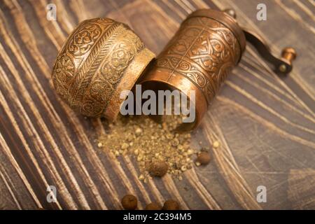 Eine offene manuelle Gewürzmühle und eine Streuung von gemahlenem Allspice auf einem Holztisch. Nahaufnahme Stockfoto