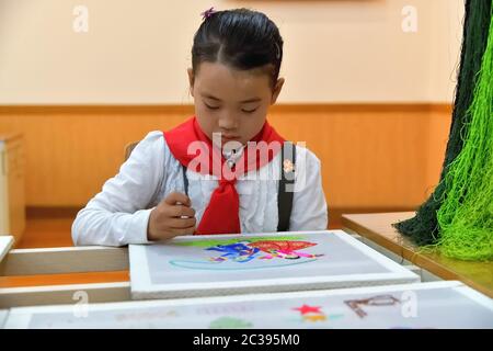 Pjöngjang, Nordkorea - 2. Mai 2019: Koreanisches Pioniermädchen stickt im Pjöngjang Palast ein Bild von Schulkindern Stockfoto