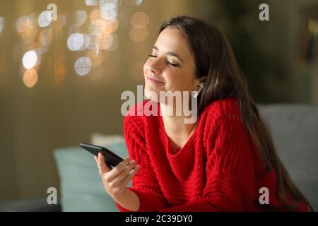Frau mit drahtlosen Kopfhörern hören und fühlen Musik von smart phone sitzen auf einer Couch in der Nacht zu Hause Stockfoto