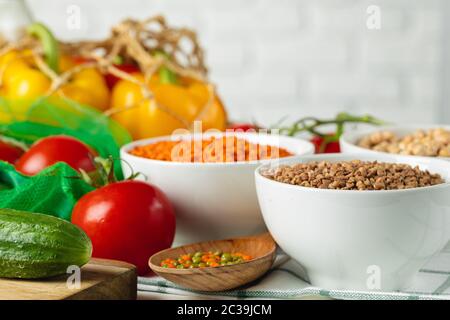 Drei weiße Schalen mit Grütze auf dem Hintergrund von frischem Gemüse Stockfoto