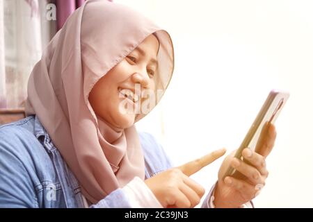 Nahaufnahme einer asiatischen muslimischen Frau mit einem Smartphone. Fröhliche lächelnde Geste gute Nachrichten bei der Kommunikation im Internet online, Videoanruf Stockfoto