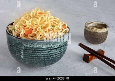 Nudelschüssel mit Karotten und Hengsten, mit Essstäbchen und Sake Stockfoto