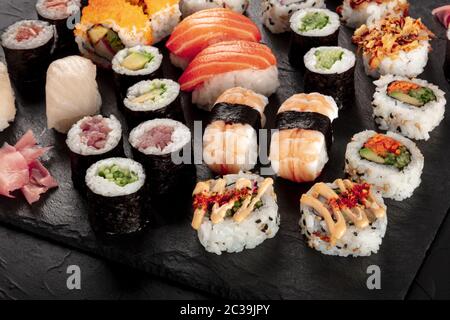 Großes Sushi auf schwarzem Hintergrund. Viele verschiedene Maki, Nigiri und Brötchen Stockfoto