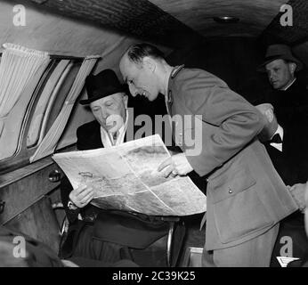 Bundeskanzler Konrad Adenauer in einem Flugzeug auf dem Weg nach Paris, rechts, bedeckt, der französische Hochkommissar Andre Francois-Poncet vor der Landung in Paris. Kurz vor der Landung übergibt ihm ein Offizier den Flugsituationsbericht mit einer großen Karte, die Adenauer mit Interesse erhält. Stockfoto