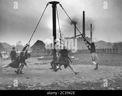 Kinder spielen auf einem Spielplatz im Ruhrgebiet. Im Hintergrund die Kamine und Rauchwolken der Industrie. Stockfoto