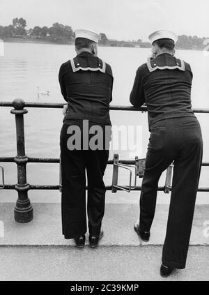 Zwei US Navy-Segler lehnen sich an ein Geländer und blicken während ihres Aufenthalts in Hamburg anlässlich eines Flottenbesuchs der US Navy in den 1950er Jahren über die Binnenalster zur Lombardsbrücke (im Hintergrund). Stockfoto