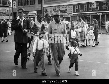 Eine afroamerikanische Familie auf einem Spaziergang auf Long Island im Bundesstaat New York. Im Hintergrund ist ein Schild: 'Folgt der Menge zu Nathans. Delicatessen Counter' und ein Geschäft 'Play 5'. Undatierte Aufnahme, wahrscheinlich aus den 50er oder 60er Jahren Stockfoto