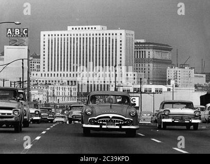 Dichter Verkehr auf dem Santa Ana Freeway in Los Angeles in den 1960er Jahren mit den typischen Karosserien der 50er Jahre. Auf der linken oberen Seite befindet sich ein Schild der ABC Brewing Company vor den Wolkenkratzern des Stadtzentrums. Dahinter, in der Mitte des Bildes, befindet sich das Federal Courthouse Building (Sitz des Los Angeles Superior Court). Rechts dahinter befindet sich das Gebäude der Justizhalle. Stockfoto