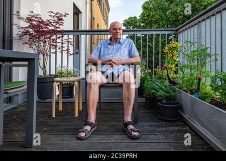 Älterer Mann, der auf dem Balkon sitzt, sieht während der Corona Pandemie in Mitte, Berlin, Deutschland nachdenklich aus - bleiben Sie während der COVID-19 Sperre zu Hause Stockfoto