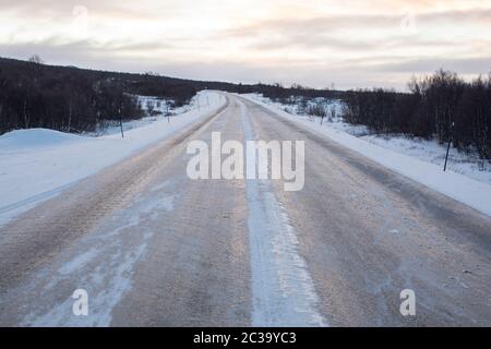 Eine gefrorene Eisstraße, die durch Bäume am Polarkreis führt. Stockfoto