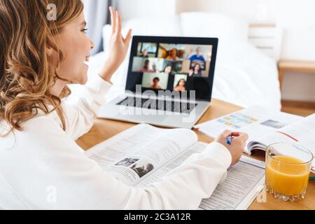 Foto von kaukasischen glücklichen Mädchen gestikulierend Frieden und mit Laptop, während Online-Studium zu Hause Stockfoto