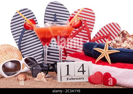 Strand-Accessoires, Muscheln, Sand, zwei Gläser mit Cocktail, rote Herzen und Kalender mit Datum 14. februar auf weißem Hintergrund. Strandparty und Urlaub Stockfoto