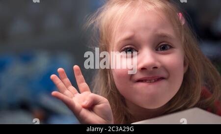 Das kleine Mädchen, das Kind lächelt und zeigt die Zahl vier mit ihrer Hand. Kleine blonde Mädchen schließen Lächeln. Stockfoto