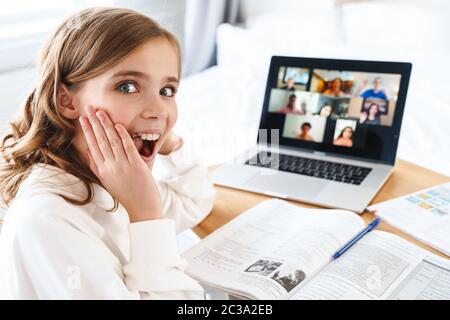 Foto von kaukasischen aufgeregt Mädchen zum Ausdruck Überraschung und mit Laptop, während Online-Studium zu Hause Stockfoto