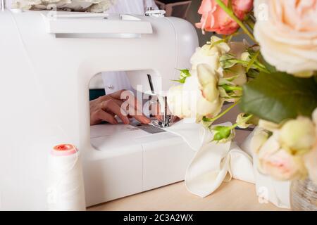 Die Näherinnen sind auf der Nähmaschine Details von Kleidung aus Stoff abgestanden. Der Meister näht neue Kleider auf die Nähmaschine. Eine Frau macht Stockfoto