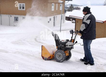 Ein Mann räumt die Straße und den Bürgersteig mit einem Schneegebläse Stockfoto