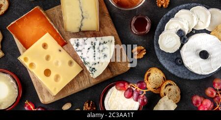 Käsepanorama auf schwarzem Blaukäse, Ziegenkäse, Brie, Emmental und anderen mit Trauben und Nüssen Stockfoto