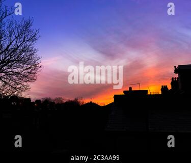 Dramatischer, lebendiger, feuerähnlicher, orange-blauer Nachthimmel und Wolken über einer starken Silhouette von Stadthäusern, Dächern und Schornsteinen in London Stockfoto