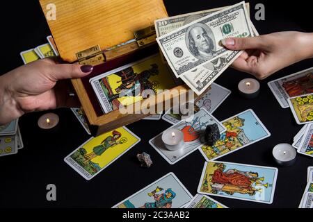 New York, USA. November 22.19. Hände halten Bargeld Dollar auf dem Hintergrund der Brieftasche und Tarot Karten. Zahlung für Esoterik, Magie und Hexerei service Stockfoto