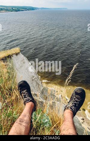 POV-Sicht der Mann sitzt auf dem Rand der Klippe mit Blick auf den Fluss Stockfoto