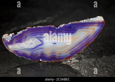 Studio-Aufnahme einer länglichen, dünnen und polierten Achatscheibe im Front- und Rücklicht mit blauen Streifen auf einer Schieferplatte Stockfoto