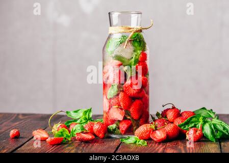 Flasche Detox Wasser hineingegossen mit frischen Erdbeeren und Basilikum. Zerstreut Zutaten auf Holztisch. Kopieren Sie Platz. Stockfoto