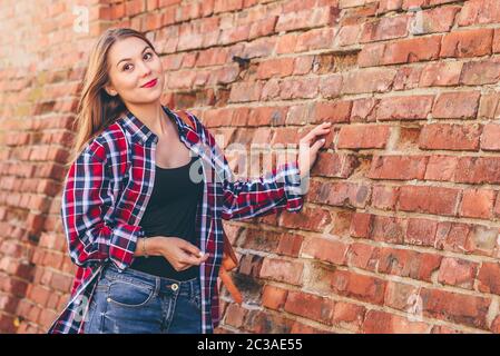 Porträt der jungen Frau im karierten Hemd und blauer Jeans gegen Mauer stehend Stockfoto