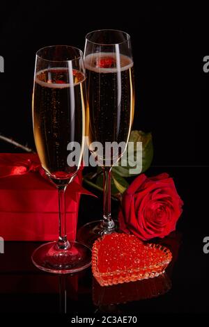 Zwei Weingläser Champagner, Geschenkbox, Rose und roter Kaviar auf Untertasse in Herzform auf schwarzem Hintergrund. Valentinstag Stockfoto