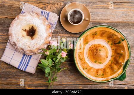 Ein Gugelhupf mit seiner Keramik-Backform und einer Tasse Kaffee und einem Feld Blumen Geburtstagsstrauß auf einem Holztisch mit einem hölzernen Hintergrund. Und eine Fi Stockfoto