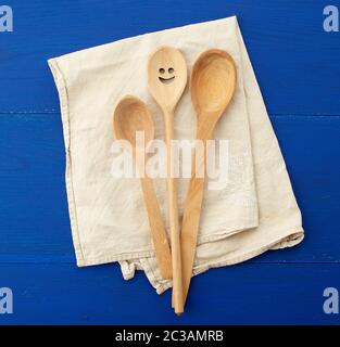 Vintage Holzlöffel und weißes Küchenhandtuch aus Textil auf blauem Holzhintergrund, Draufsicht Stockfoto