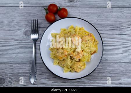 Italienische Pasta in cremiger Soße mit Garnelen auf dem Teller, Draufsicht. Pasta in Form von Bögen auf Holzgrund Stockfoto