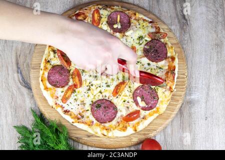 Frauenhand mit einem Messer schneidet Pizza auf einem runden Brett Stockfoto