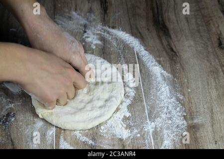 Frauenhände machen auf einem Holztisch ein Fladenbrot für Pizza Stockfoto