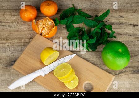 Zitronen mit Minze und drei Orangen auf einem Holzbrett in Scheiben geschnitten Stockfoto
