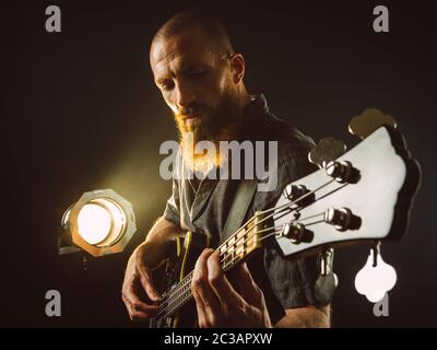 Foto eines bärtigen Mannes spielte Bass Gitarre auf der Bühne vor der Strahler. Stockfoto