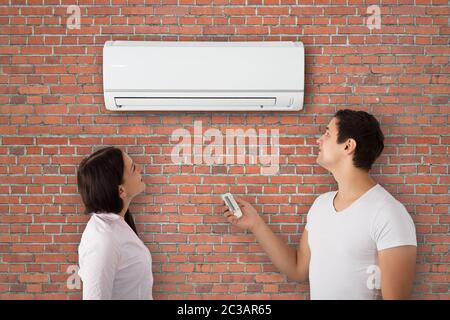 Junges Paar Einschalten der Klimaanlage mit Fernbedienung An Wand Stockfoto