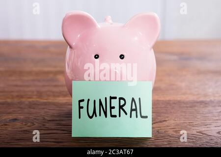 Beerdigung Plan auf einem selbstklebenden Hinweis in der Nähe von Rosa Sparschwein über strukturierte Holzoberfläche geschrieben Stockfoto