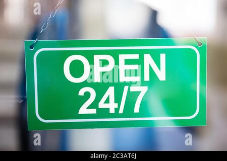 In der Nähe von Grün rund um die Uhr geöffnet Information Board hängend auf Glas Tür Stockfoto