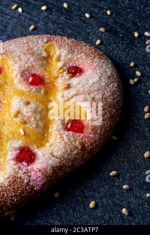 Nahaufnahme eines Coca de Sant Joan, ein typischer süßer flacher Kuchen aus Katalonien, Spanien, gegessen an der St. Johns Eve, auf einer schwarzen Stoffoberfläche mit pi bestreut Stockfoto