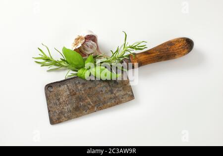 Altes rostiges Fleischspaltmesser mit frischem Basilikum und Rosmarin Stockfoto